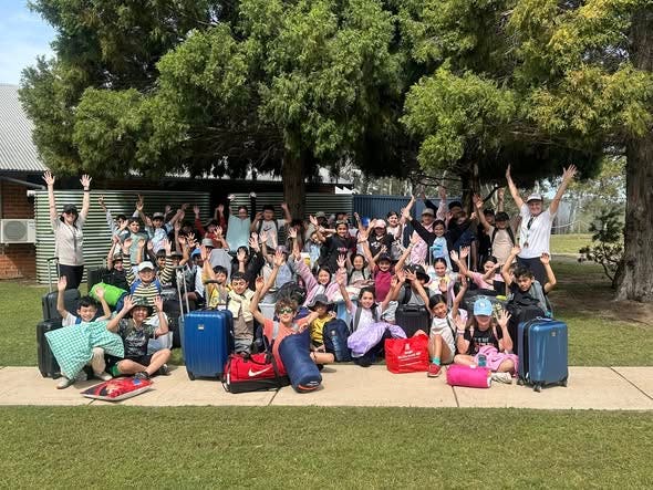 photo of a large group of students and teachers at school camp, smiling with thier hands in the air.